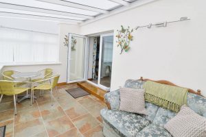 Conservatory room at Carnavis Cottage with table and chairs, sofa and doors leading to house