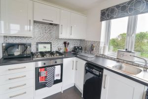 Well equipped kitchen with garden views through window at Carnavis Cottage