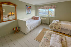 Triple bedroom at Penamont with 3 single beds, window to the front of the house. Painted floor with rug in between single beds and wall mounted large mirror.