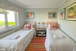 Twin bedroom at Penamont with bedside table and lamps in between the beds and rug. Window to the rear garden
