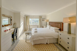 Superking ensuite bedroom at Penamont with bedside tables and lamps. Wooden painted floor with rug and window to the front of the house