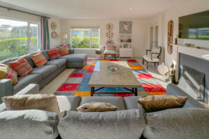 Lounge at Penamont from the hallway door with large windows to the front and side of the house and fireplace with TV over the mantel. Wooden painted floor with large rg