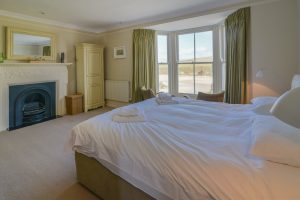 First floor master bedroom with superking bed, feature fireplace and bay window overlooking the beach at Santa Marina