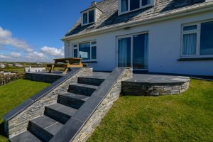 The patio with picnic table and slate steps to the lawn area