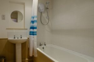 Bathroom off the hallway with electric shower over the bath and toilet and wash basin