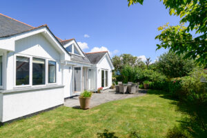 Rear exterior of Tregarne with outside dining furniture on the patio with double doors leading into the lounge