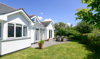 Rear exterior of Tregarne with outside dining furniture on the patio with double doors leading into the lounge