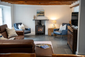 Lounge area with corner sofa, TV log burner, oak beams at Carrek Cottage