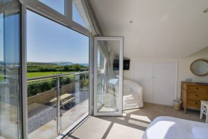 Large glass doors in the master ensuite bedroom with Juliet balcony and view toward Trevose Head over countryside and ocean