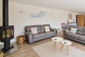 Open plan lounge area with comfortable seating and wood burner at Trebriani