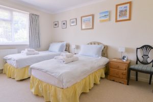 One of two twin rooms at Tamarisk with bedside tables, large window and picture on the wall. This bedroom shares an ensuite with the second twin bedroom