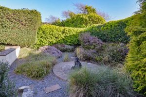 Rear garden area at Tamarisk with plants, round patio area with statue