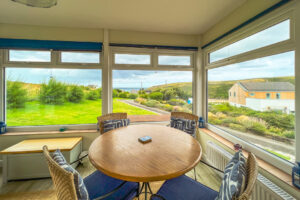 Sun room at 't Sandt with table and chairs and other seating with view over the garden, driveway and out to sea