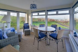 Sun room at 't Sandt with table and chairs and other seating with view over the garden, driveway and out to sea