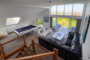 The second floor living room from the third floor living room showing ample seating, pool table, floor to ceiling windows and large sliding doors onto the balcony
