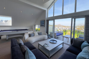 The living room on the second floor at Tristan featuring a pool table, comfortable seating and large glass doors onto the balcony