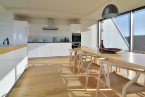 The dining table and chairs in the open plan kitchen and dining area at Spin with views from the large windows to the side of the house towards the coast and ocean