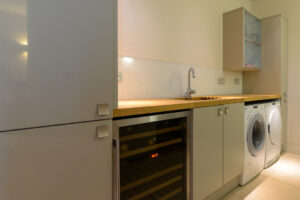The utility area on the ground floor level with sink, washing machine and tumble dryer. This room is access by steps from the living area to the entrance hall and is opposite the entrance way