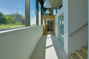 The hallway on the lower ground floor at Spin with stairs to the lounge area, large windows running the length of the hallway and doors to the bedrooms on the lower floor