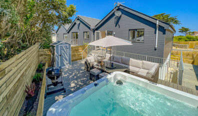 Rear exterior view of the decking at No 1 Treglos Gardens with seating, BBQ and hot tub