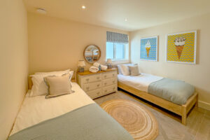 The single beds in the second of the two ground floor twin bedrooms at Tremblaze with pictures on the wall and chest of drawers with lamps