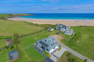 High aerial view over Tremblaze and neighbouring property out over the beach at Harlyn Bay and the ocean