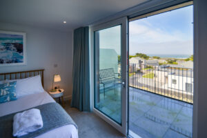 The first floor king bedroom with large sliding doors onto the balcony and views over neighbouring properties towards the ocean and Trevose Head