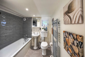 Toilet, wash hand basin and bath with hand held shower in bathroom 1 at No 8 Sandhills