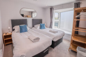 Bedroom 2 at No 2 Treglos with twin beds, mirror above the bed and free-standing hanging space for clothes.