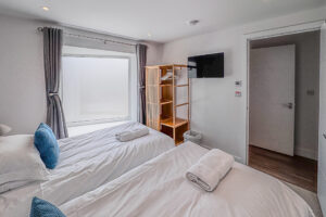 Bedroom 2 at No 2 Treglos with twin beds, wall-mounted television and free-standing hanging space for clothes.
