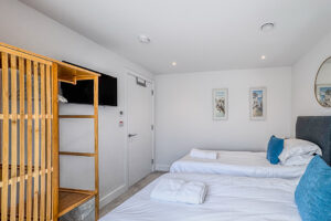 Bedroom 2 at No 2 Treglos with twin beds, wall-mounted television and free-standing hanging space for clothes.